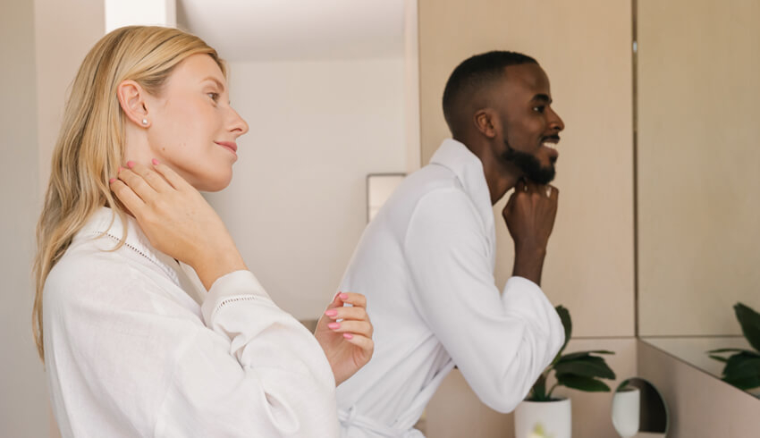 A man and woman standing in front of a bath room mirror while cleansing their skin